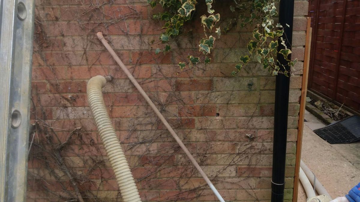 Inblaasslang aangesloten op een geboord gat in een bakstenen gevel, tijdens het vullen van de spouw